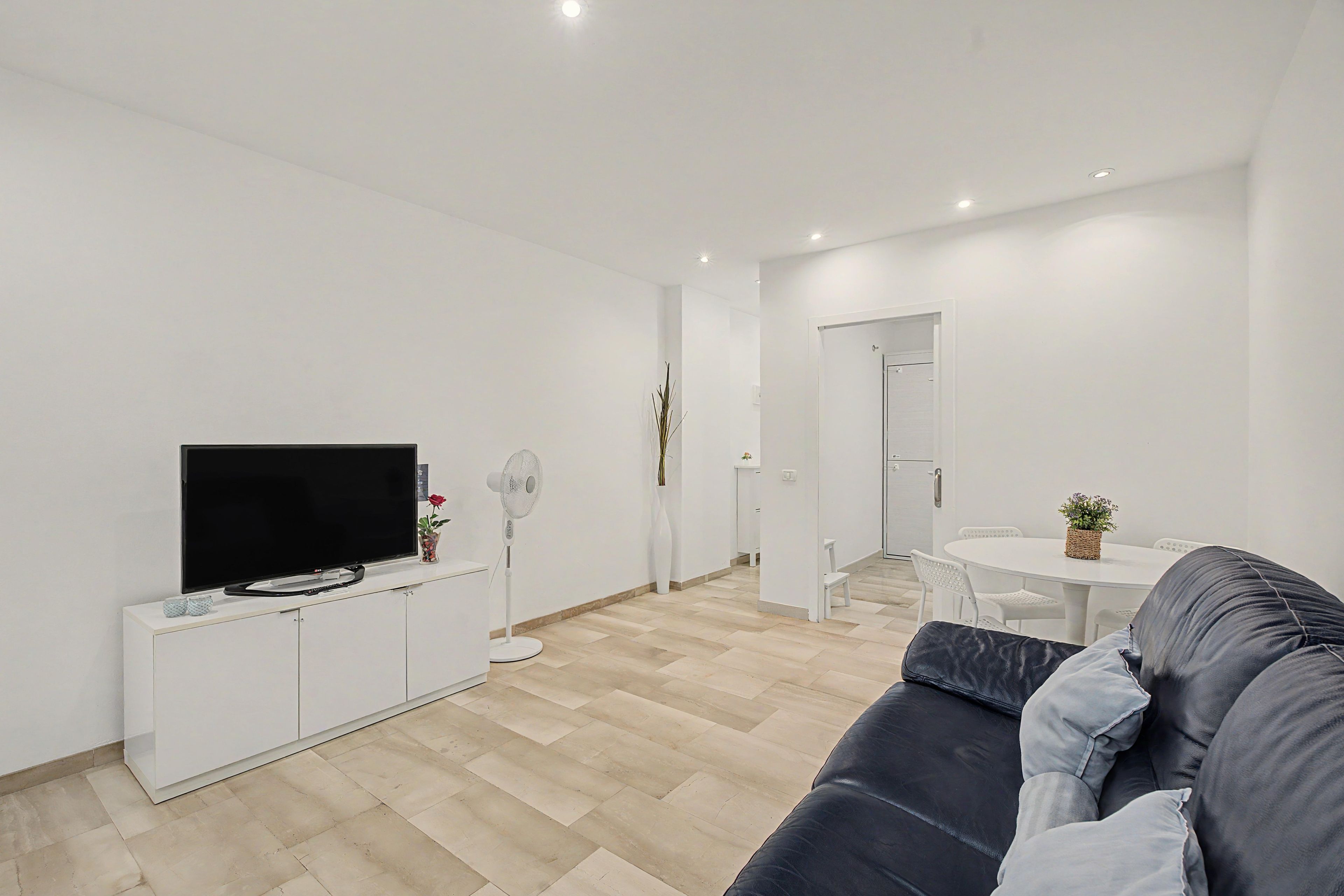 En moderne stue med et fladskærms-tv, et hvidt tv-møbel, en sort sofa og et spiseområde med et rundt bord og stole.