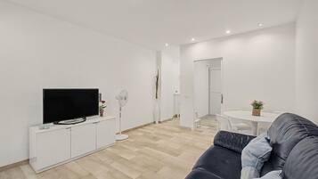 En moderne stue med et fladskærms-tv, et hvidt tv-møbel, en sort sofa og et spiseområde med et rundt bord og stole.