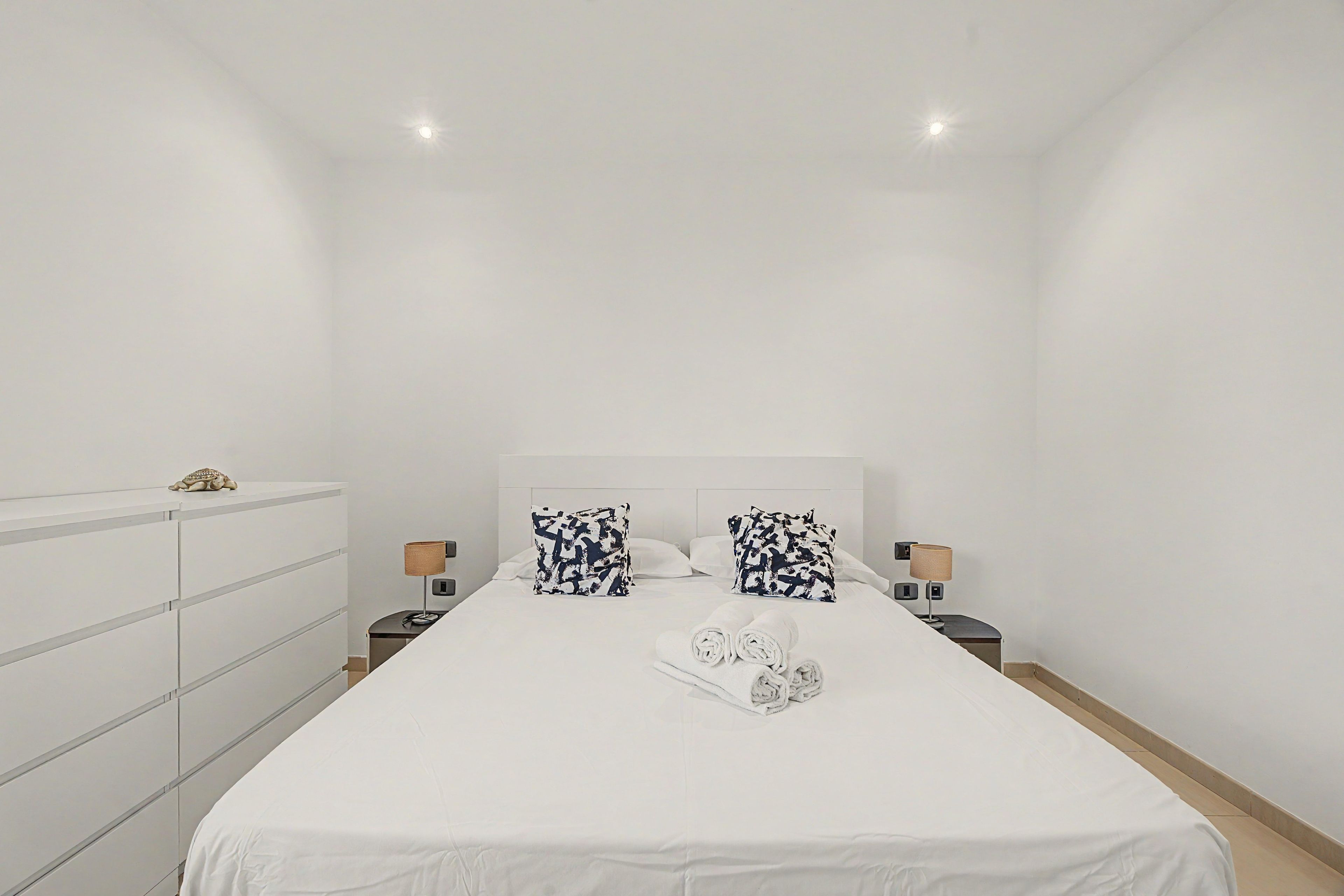 Een hotelkamer met een groot bed, twee nachtkastjes met lampen, een dressoir en een plafondlamp.