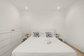 Une chambre d’hôtel avec un grand lit, deux tables de chevet avec des lampes, une commode et un luminaire au plafond.