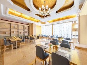 Un vaste espace dédié à la salle à manger, comprenant plusieurs tables et chaises, un lustre et une grande fenêtre agrémentée de rideaux.