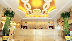 A hotel lobby with a reception desk, two receptionists, a chandelier, and large potted plants. - Vienna Hotel Guangzhou Airport (Guangzhou)