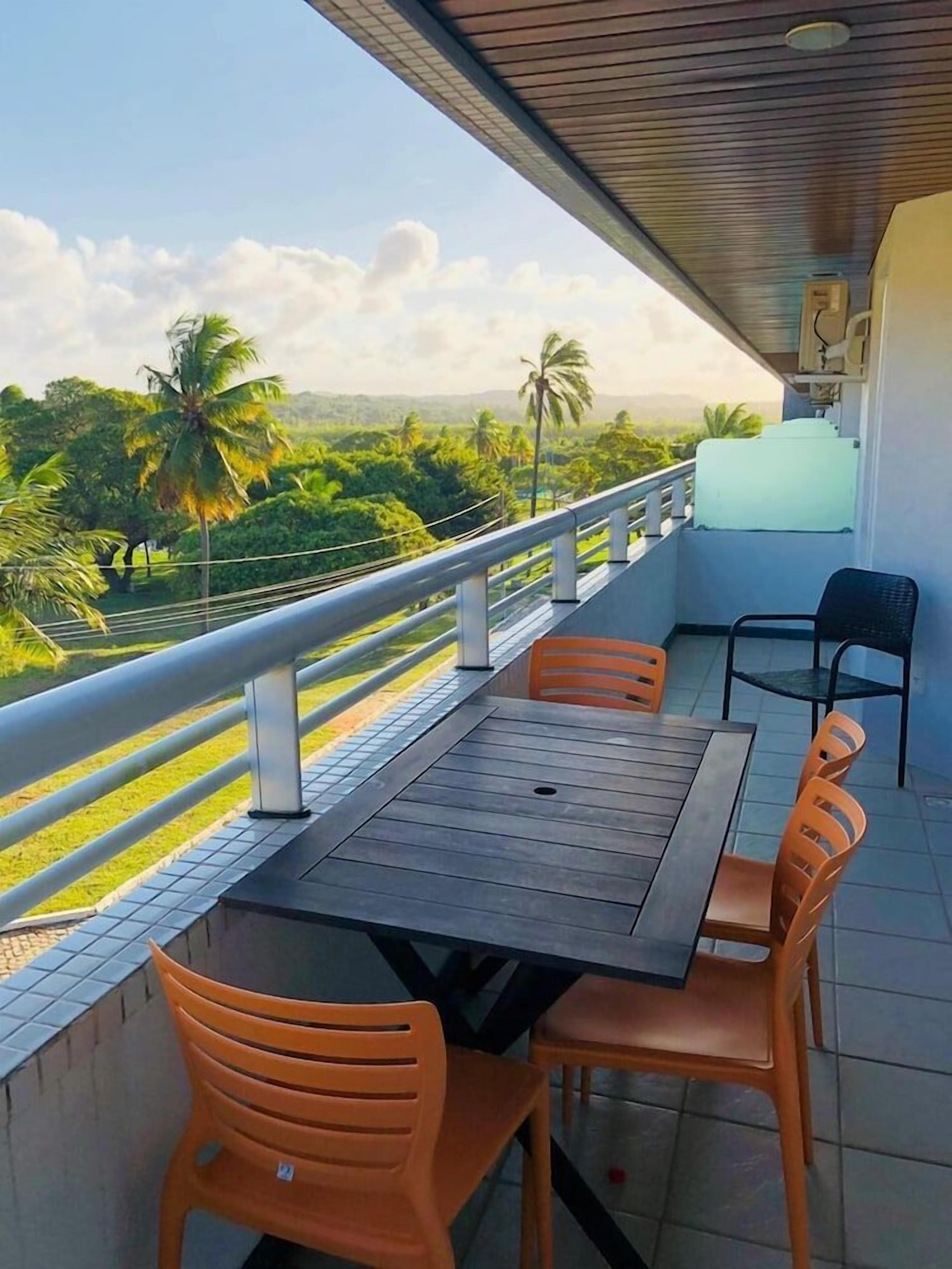 Uma varanda com mesa e cadeiras, com vista para um jardim com palmeiras.