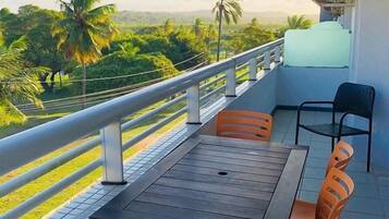 Uma varanda com mesa e cadeiras, com vista para um jardim com palmeiras.