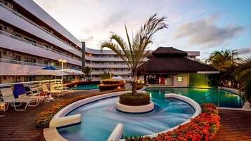 Um hotel com piscina, espreguiçadeiras e uma estrutura com telhado de palha.