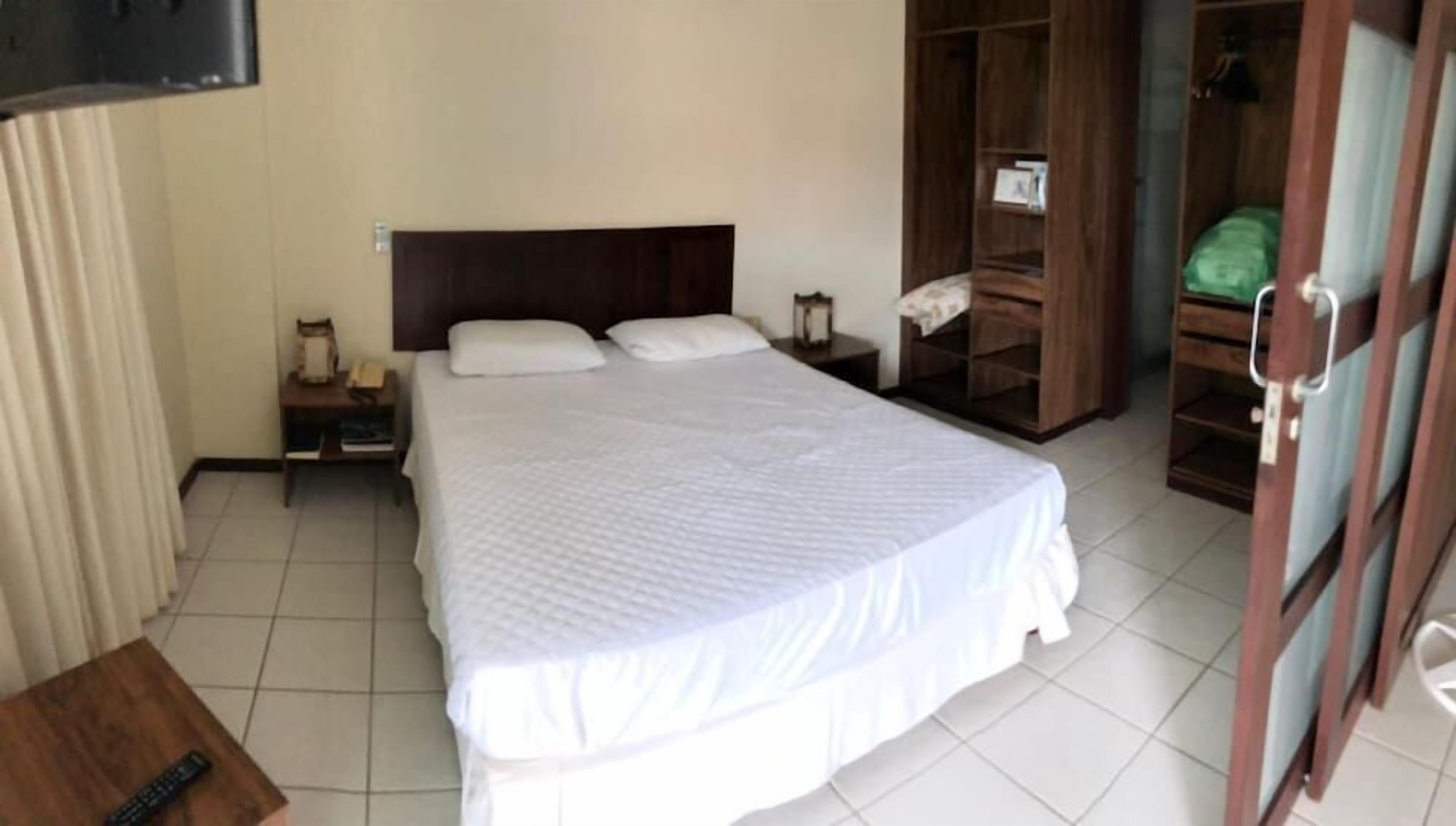Quarto de hotel com cama, mesas de cabeceira, armário e televisão.