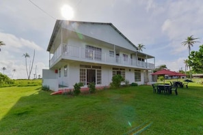 A two-story building with a balcony, surrounded by a grassy area and palm trees. - Apartamentos Hermanos Morales Merino (San Andrés)