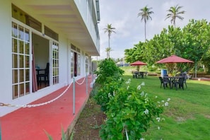 A hotel with a red carpeted entrance, outdoor seating with red umbrellas, and palm trees in the background. - Apartamentos Hermanos Morales Merino (San Andrés)