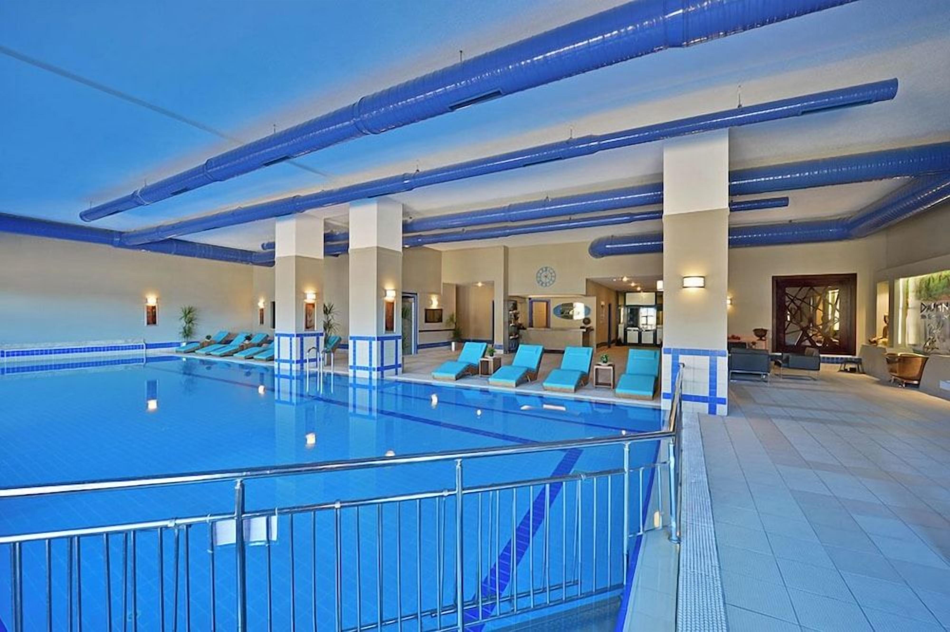 Una piscina interior con varias pistas, sillas de descanso y una zona de recepción.