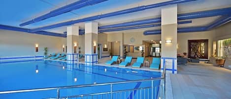 An indoor swimming pool with multiple lanes, lounge chairs, and a reception area.