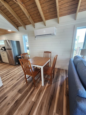 A dining area with a wooden table and chairs, a kitchen with a refrigerator, and a window with a view.