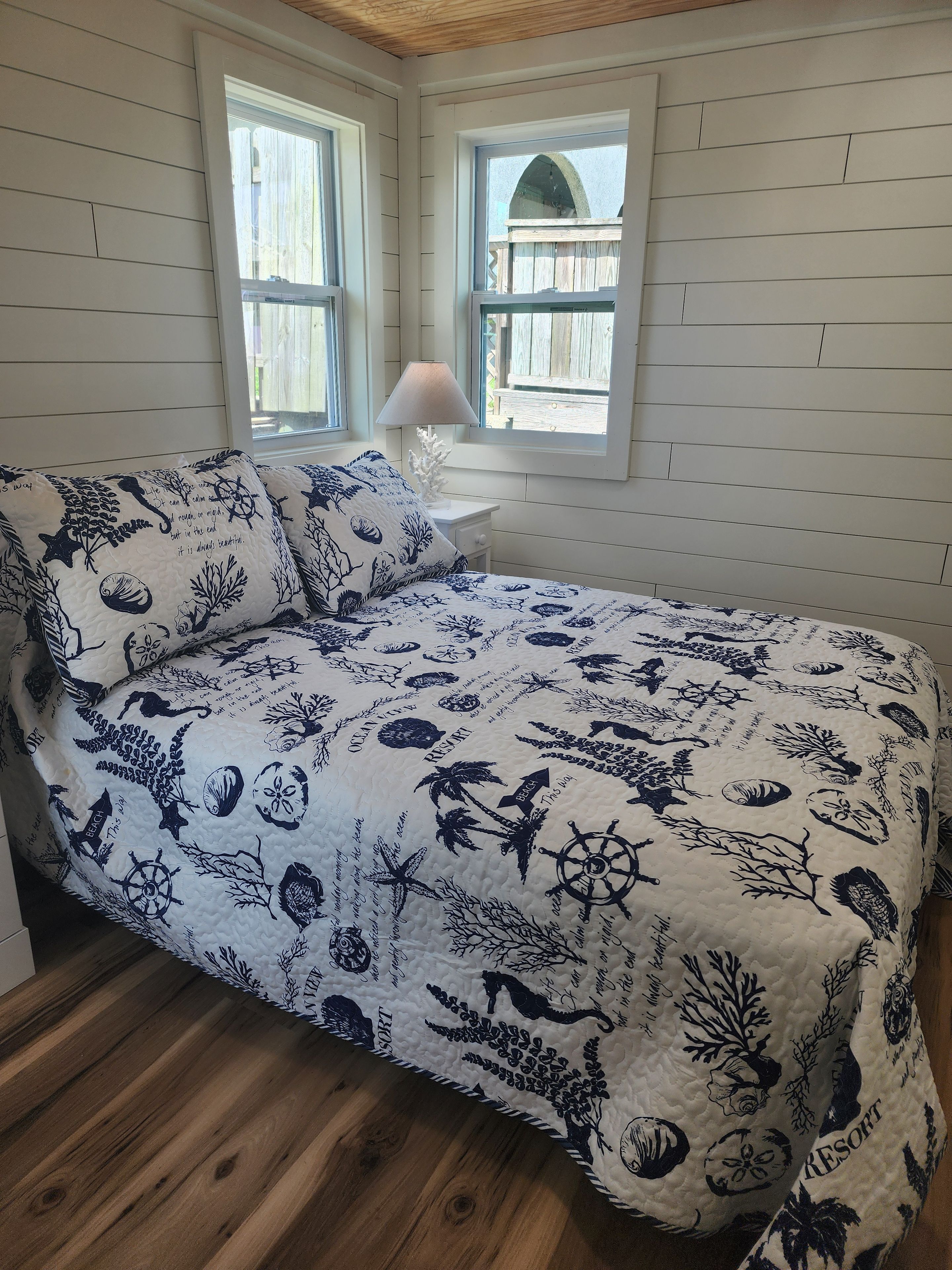 Une chambre à coucher avec un lit, deux fenêtres, une table de chevet et une lampe.