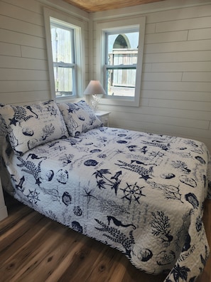 A bedroom with a bed, two windows, a nightstand, and a lamp.