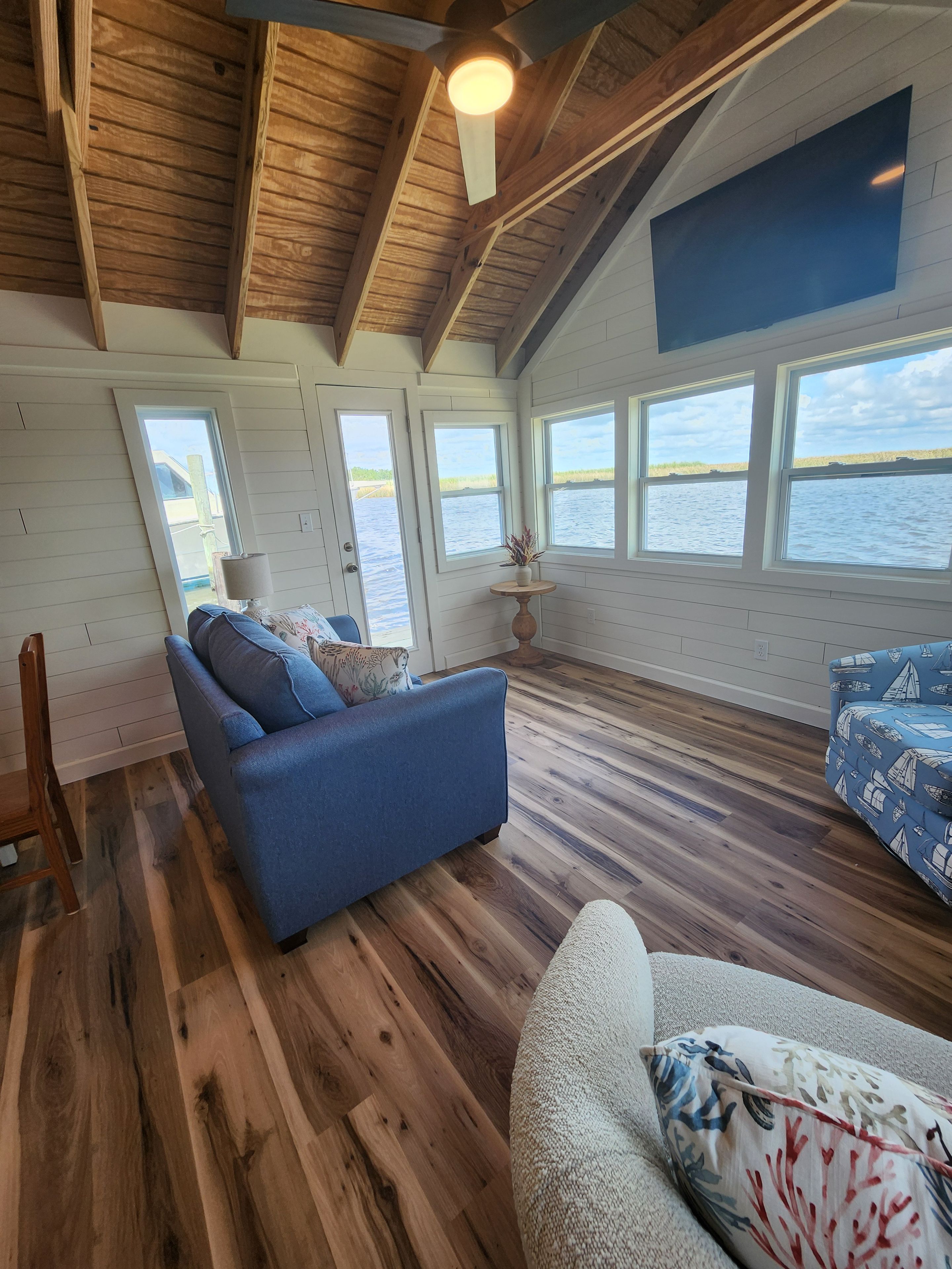 L'intérieur d'une cabine avec un canapé bleu, un fauteuil blanc, un plancher en bois et une vue sur l'eau par de grandes fenêtres.