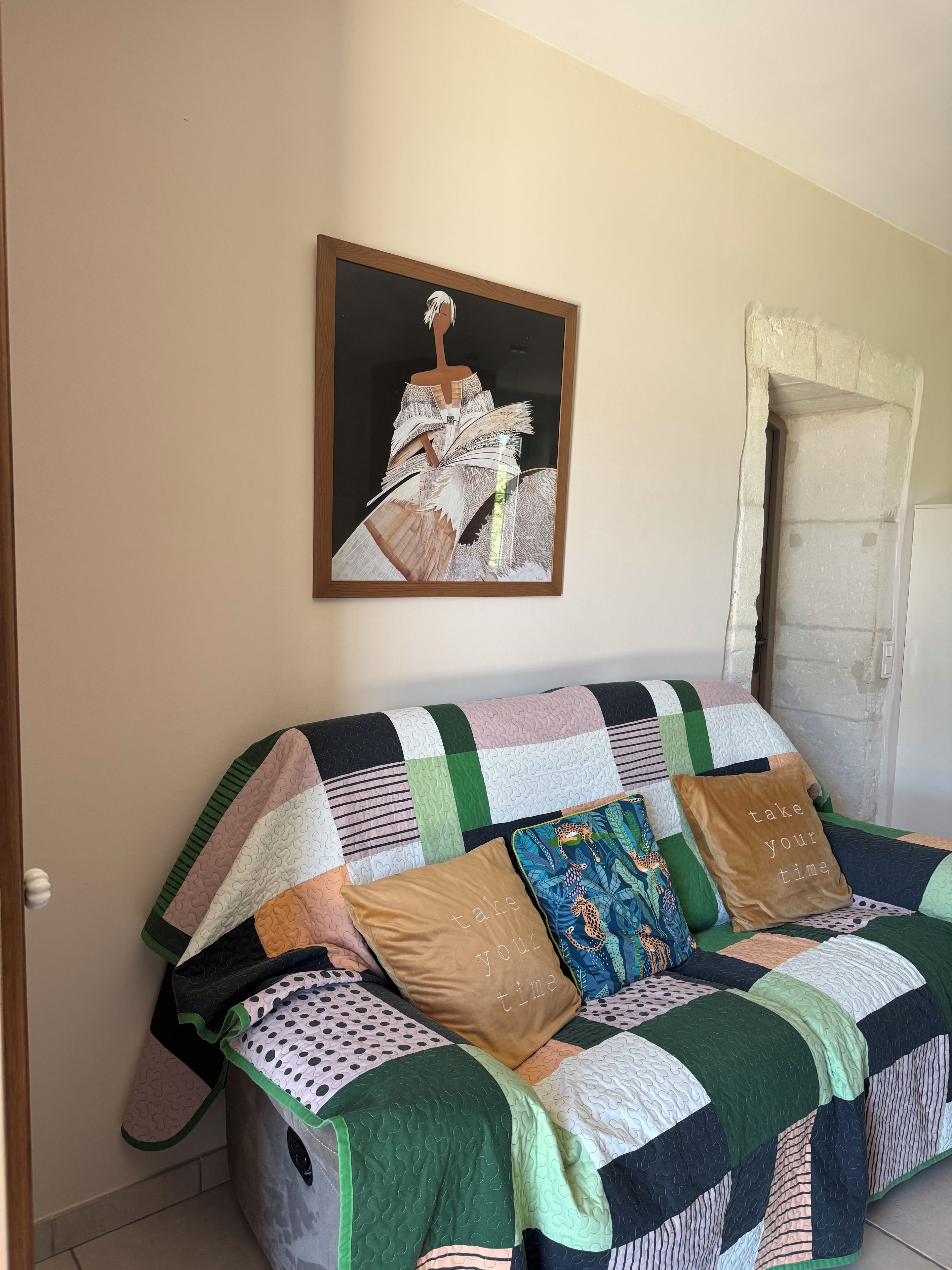 Een kamer met een bank, bekleed met een lappendeken, een kunstwerk erboven en een deur met een ruwe textuur.