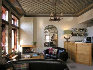 Een knusse woonkamer met een open haard, een barruimte met flessen op planken, en een comfortabele zithoek.