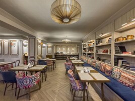 Un restaurante con una larga mesa compartida, cabinas individuales y una estantería con libros y objetos decorativos.