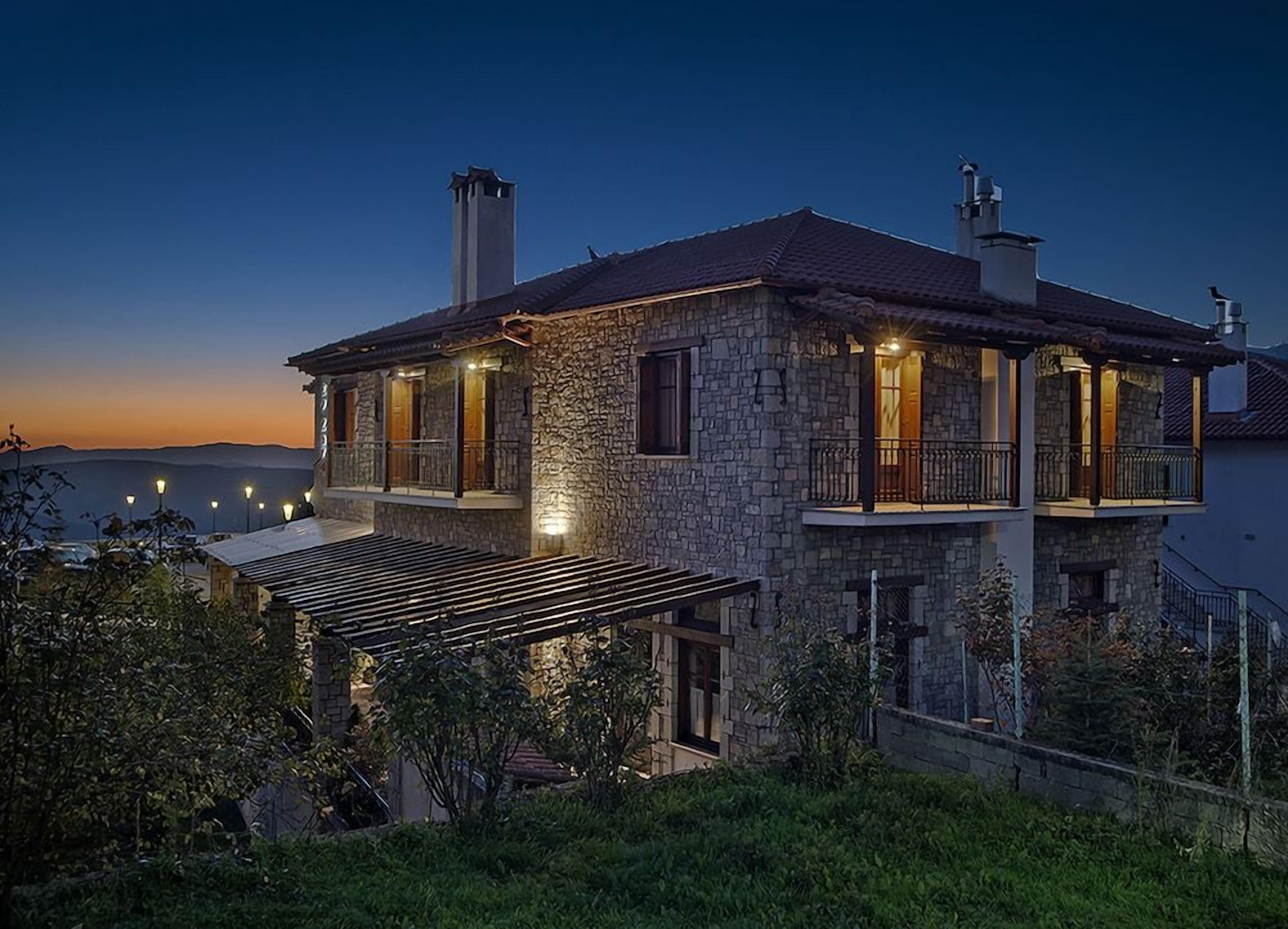 A stone house with a balcony, a covered patio, and a view of the sea at dusk.