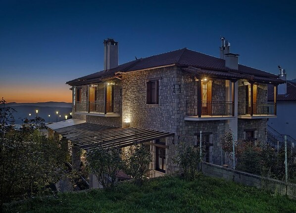 Een stenen huis met een balkon, een overdekte patio en uitzicht op zee in de schemering.