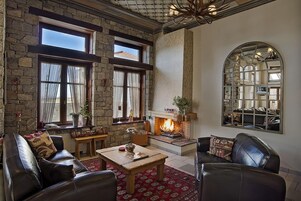 Una sala de estar acogedora con chimenea, paredes de piedra, muebles de cuero y ventanas amplias.