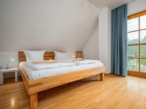 A bedroom with a wooden bed, white bedding, a nightstand with a lamp, and a window with curtains. - 10a/t6 Holiday Park "freesenbruch" (Zingst)