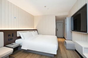 Una habitación de hotel moderna con una cama grande, mesitas de noche, un televisor de pantalla plana y un vestidor.