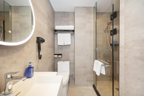 Een moderne badkamer met een douchecabine van glas, een wit toilet, een wastafel met spiegel en een haardroger aan de muur.