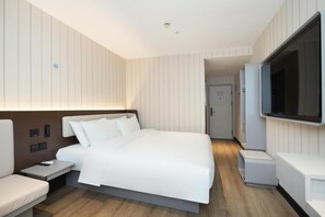 Een moderne hotelkamer met een groot bed, nachtkastjes, een televisie en een deur naar een andere kamer.