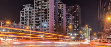 A nighttime cityscape with high-rise buildings and light trails from moving vehicles.