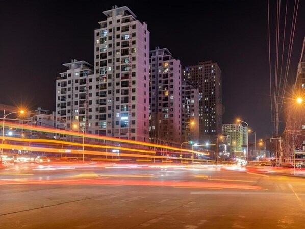 Un paisaje urbano nocturno con rascacielos y estelas de luz dejadas por vehículos en movimiento.