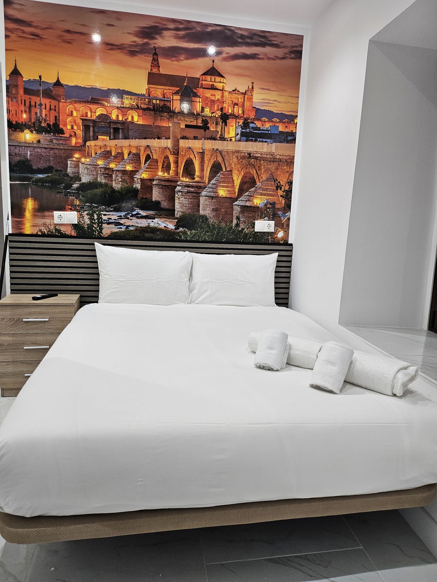A hotel room with a large bed, a view of a historic building, and a night sky.