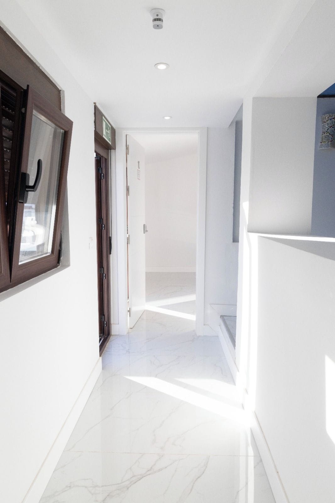 A hallway with a marble floor, a door on the left, and a staircase on the right.