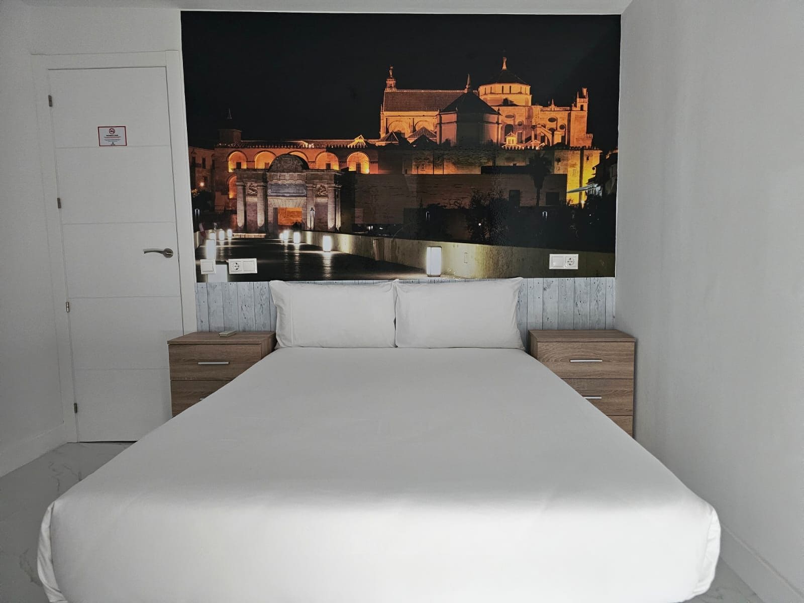 Un dormitorio con una cama grande, dos mesitas de noche y un tapiz que representa un edificio histórico de noche.