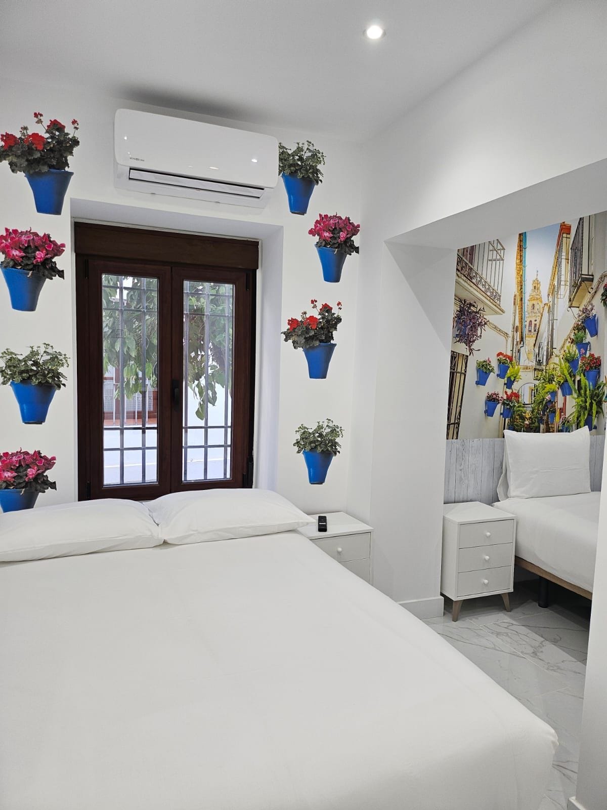 Un dormitorio con cama, mesita de noche, aire acondicionado de pared y plantas en macetas.