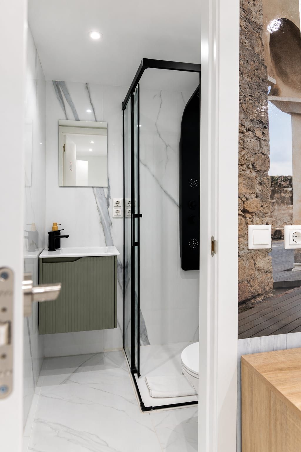 Un baño moderno con ducha envuelta en vidrio, piso de baldosas de mármol y tocador de madera.