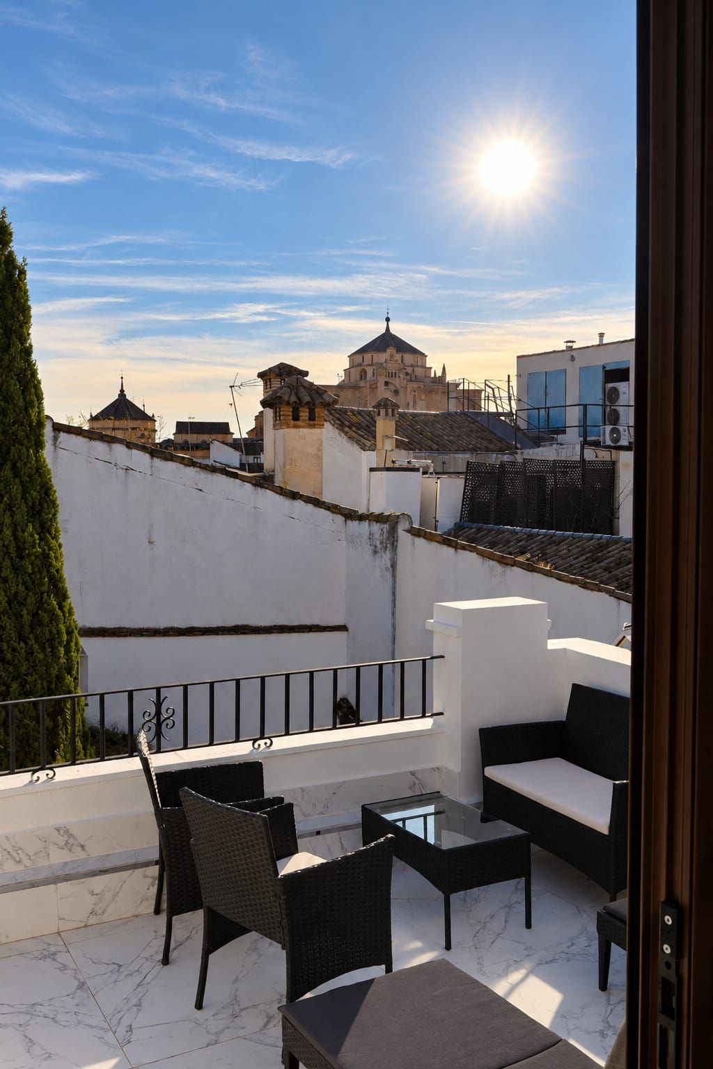 Una terraza en la azotea con mobiliario exterior, cielo despejado y vistas a edificios históricos.