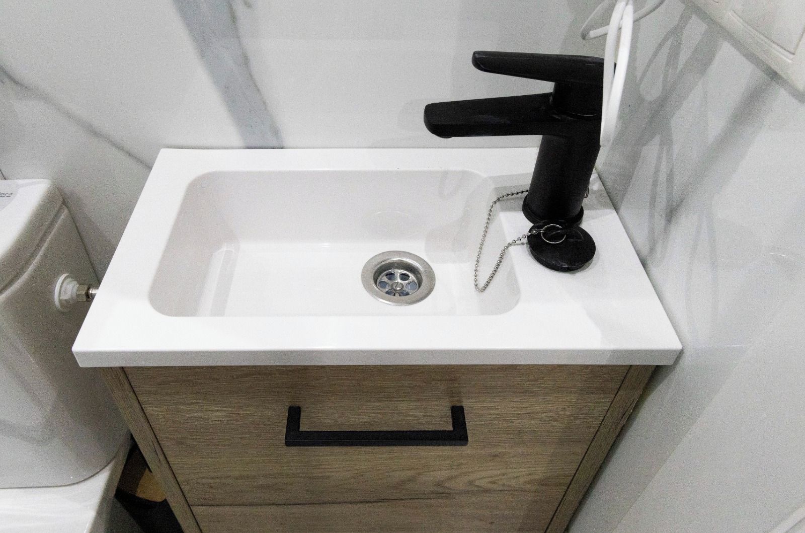 A bathroom with a white sink, black faucet, and a wooden cabinet with a drawer.