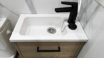 A bathroom with a white sink, black faucet, and a wooden cabinet with a drawer.