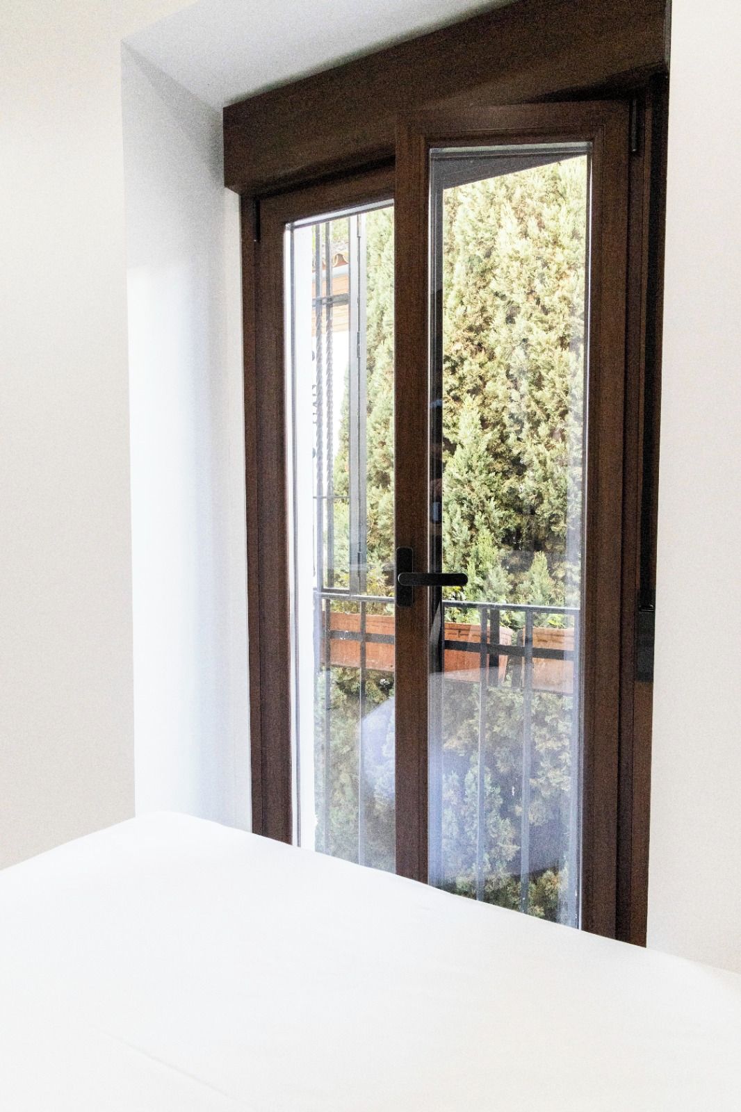 Una habitación con un ventanal grande, un techo blanco y vistas a un balcón con barandilla.