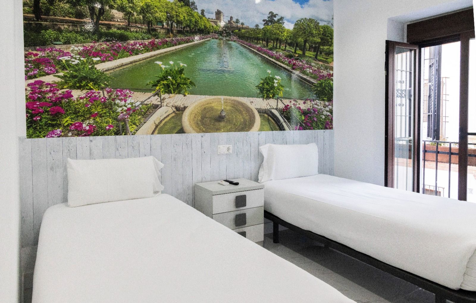 Habitación de hotel con dos camas, una mesita de noche pequeña y un ventanal grande.