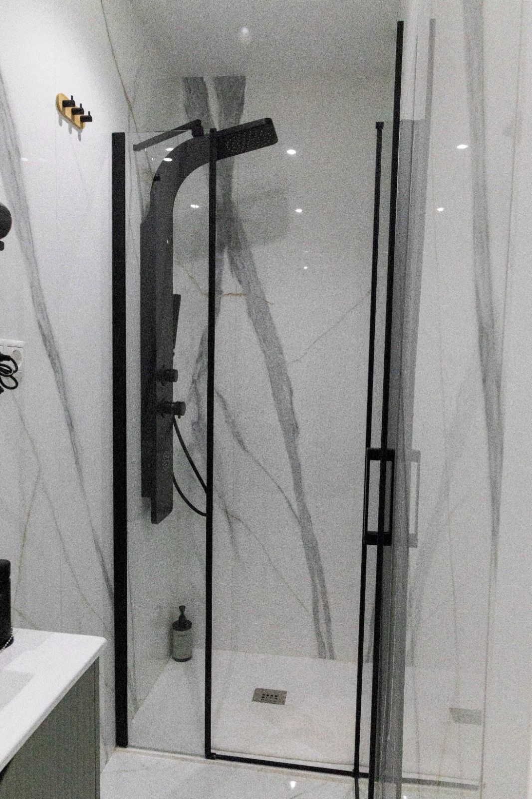 Un baño moderno con cabina de ducha de vidrio, pared de mármol blanco y toallero negro.