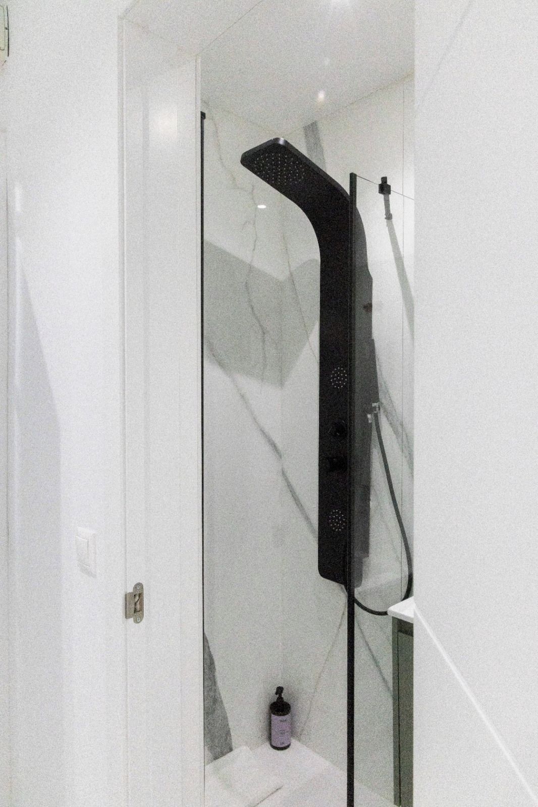 A modern bathroom with a glass shower enclosure, a white marble wall, and a small bottle on the floor.