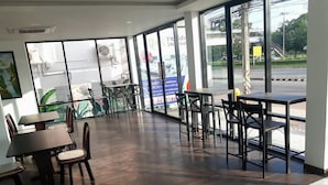 Ett rymligt inomhusområde med flera bord och stolar, stora fönster och utsikt  över gatan utanför.