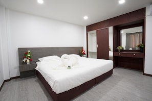 A modern hotel room with a large bed, a bedside table with a vase of flowers, a dresser with a mirror, and a large mirror above the dresser. - NK Residence Sakon Nakhon (Sakon Nakhon)