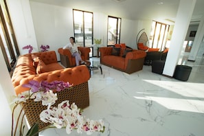 A spacious living area with a sofa, a chair, and a hanging chair. There is a glass coffee table and a potted plant. - NK Residence Sakon Nakhon (Sakon Nakhon)