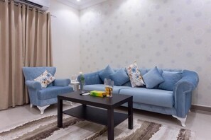 Un salon avec un canapé bleu, deux fauteuils, une table basse et un mur orné d’un motif.