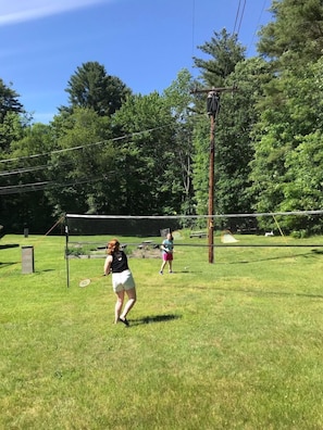 An outdoor tennis court with a net, surrounded by trees and a grassy area. - The Briarcliff Motel (Great Barrington)