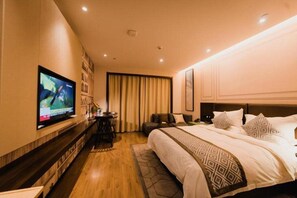 Una camera d'albergo con un letto grande, una televisione a parete, una scrivania con una sedia e una finestra con tende.