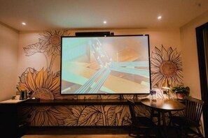 A room with a large flat-screen TV mounted on the wall, a wooden bar counter with a leaf pattern, and a round dining table with chairs.