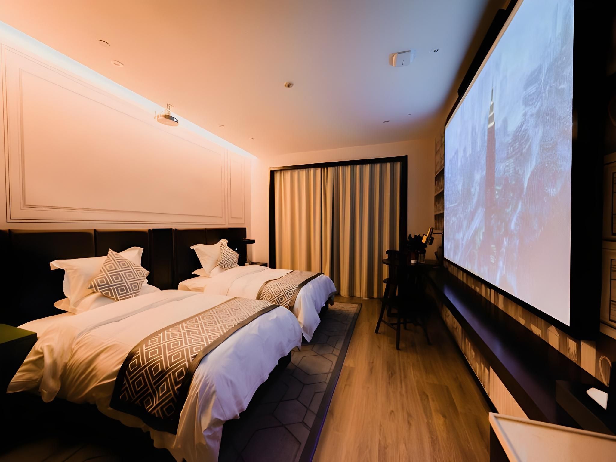 Habitación de hotel con dos camas, una pantalla grande y un escritorio con una silla.